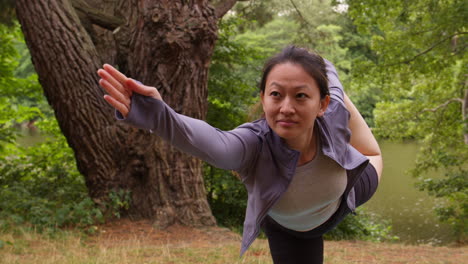 woman wearing sports clothing doing yoga stretching and balancing in forest by lake or river enjoying peace and beauty of nature 1