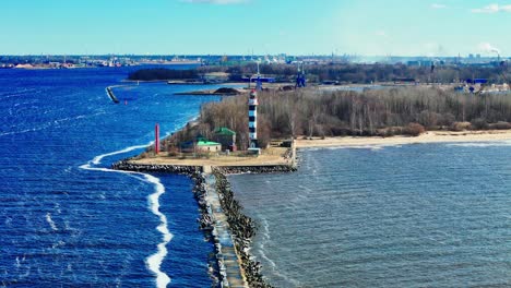 aerial footage shows a striped lighthouse at the end of a long jetty, flanked by leafless trees and distant city buildings along the waterfront