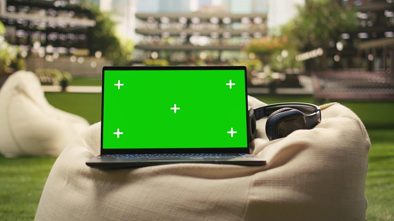 Mockup di laptop con schermo verde posizionato su un pouf all'aperto con cuffie