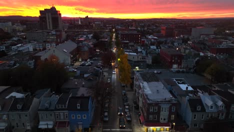 Descending-aerial-view-of-cars-driving-on-city-street-with-beautiful-autumn-sunset-on-horizon