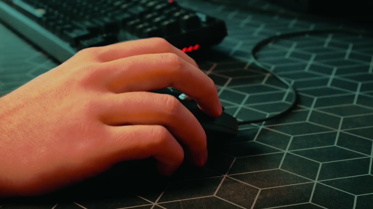 Close-up of a hand operating a computer mouse on a patterned desk surface, with a keyboard visible in the background, capturing everyday computer work in an indoor office setup