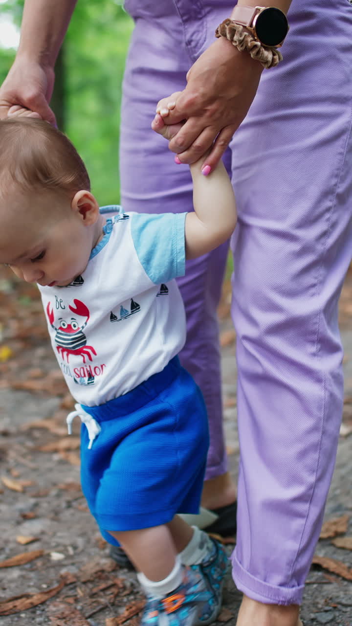 Curious sweet baby boy walking with mom's help. Lovely kid stepping and looking down with interest. Nature backdrop. Vertical video