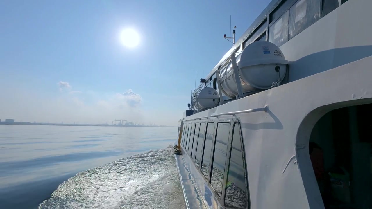 Ich-Perspektive vom Deck einer fahrenden Fähre, die eine klare, weiße Schaumkielwelle und eine ferne Stadtsilhouette entlang einer wichtigen Schifffahrtsroute in der Straße von Singapur zeigt.