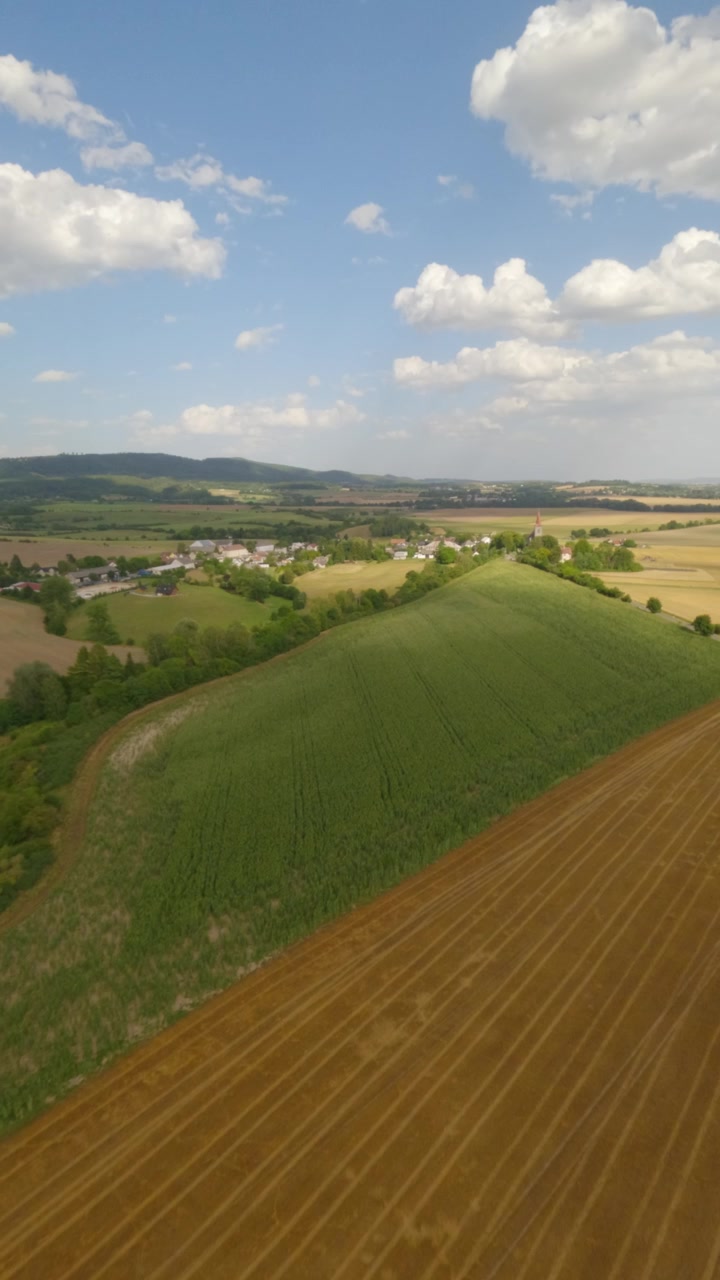 A vertical aerial perspective showing lush green fields, harvested golden farmland, and a distant village in the Czech Republic. Ideal for travel and nature social media content.