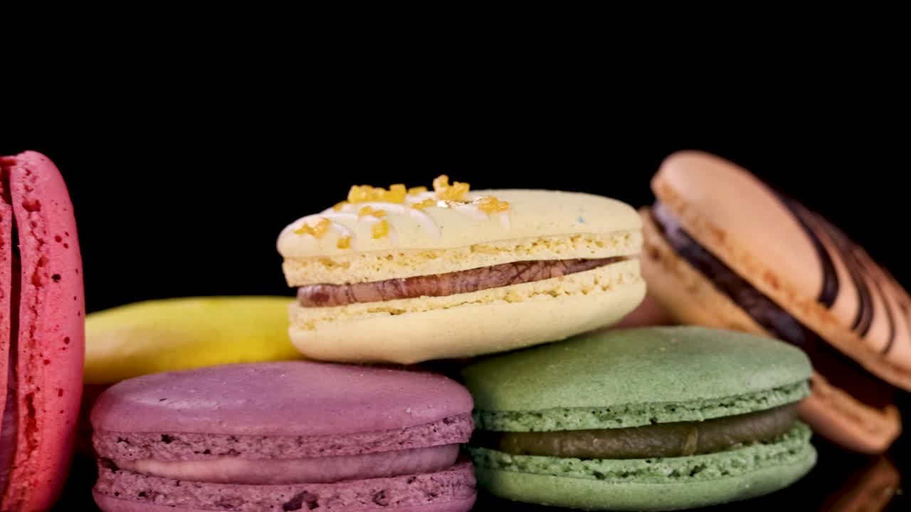 A vibrant selection of assorted French macarons rotates smoothly on a glossy black surface, illuminated by soft studio lighting for a vivid, appetizing effect