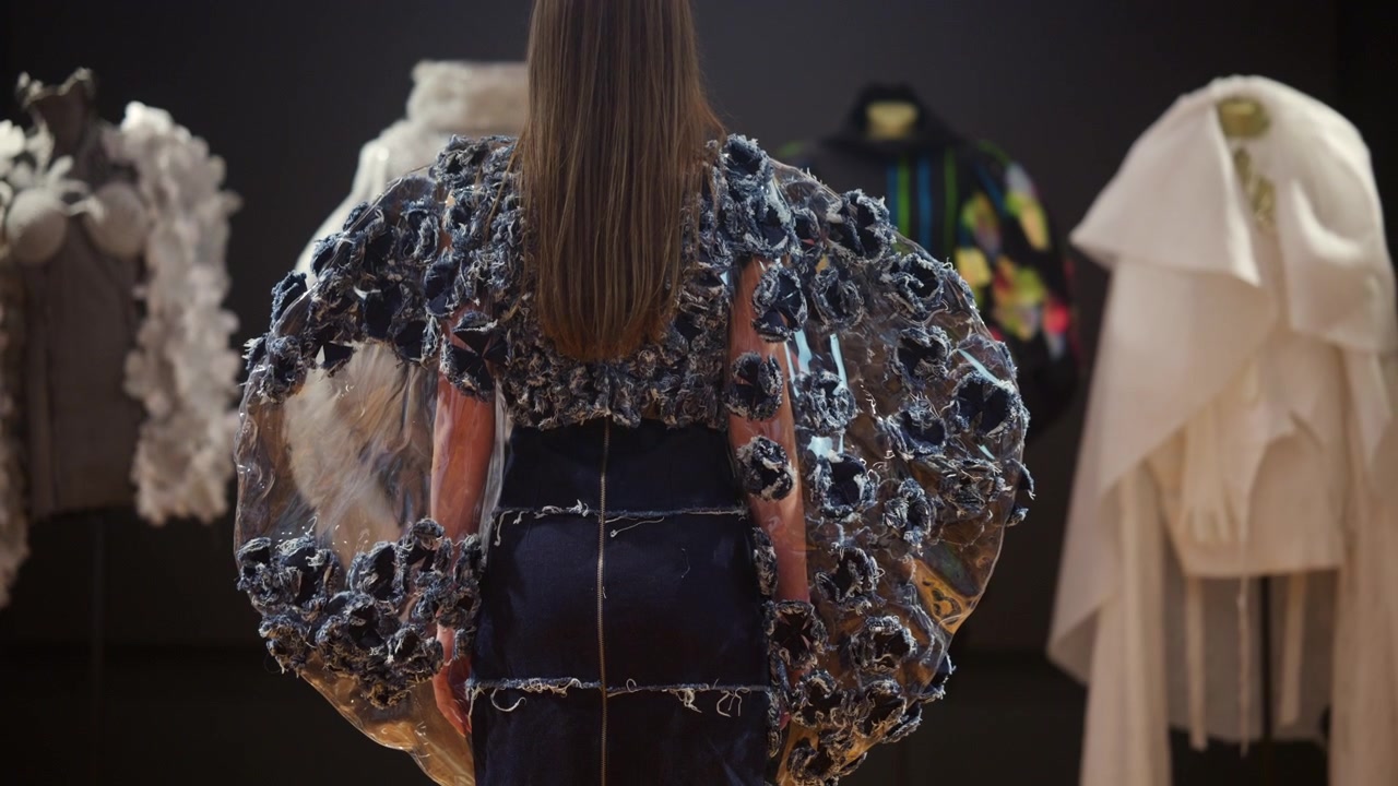 Vista de uma modelo usando um vestido avant-garde com elementos de tecido azul texturizado e mangas transparentes e amplas