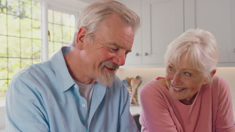 Lächelndes-älteres-Ehepaar-Im-Ruhestand,-Das-Zu-Hause-In-Der-Küche-Sitzt-Und-Ein-Finanzdokument-Unterzeichnet