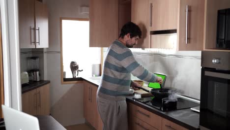 main view of a man with stripped jersey using a tablet for cooking at the kitchen while following a recipe from the internet