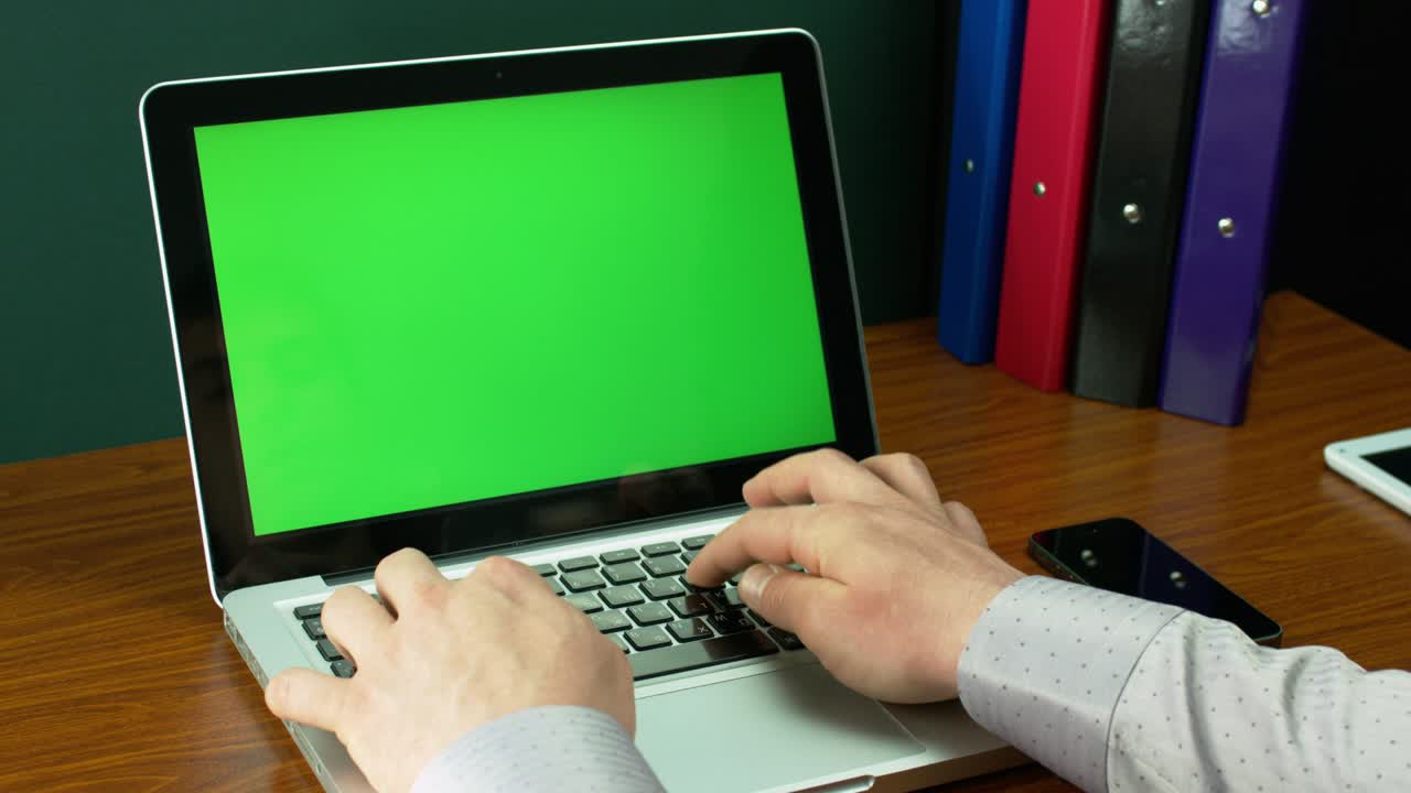 un hombre de negocios con una camisa marrón claro escribiendo en una computadora portátil con pantalla verde.