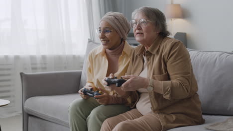 happy middle aged arabic woman and senior lady playing video game together and having fun while sitting on sofa at home 1