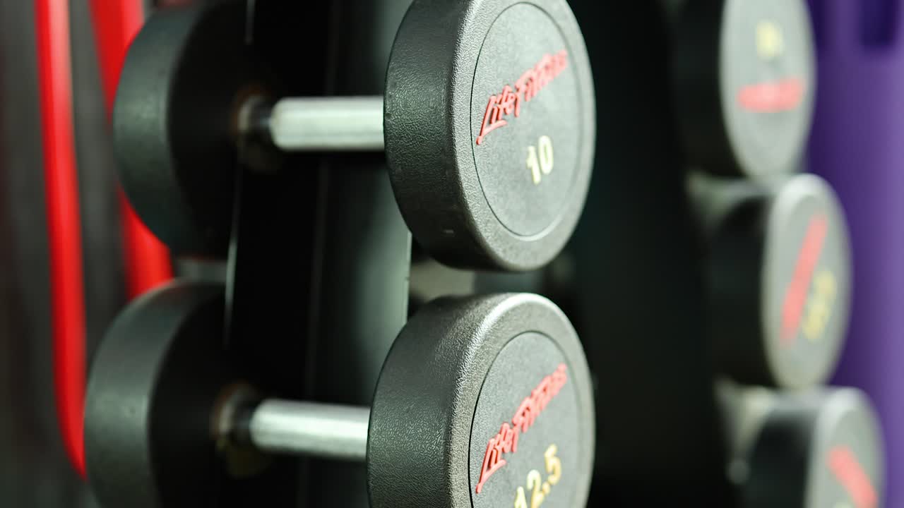 A series of dumbbells on a rack in a colorful gym environment with bright lighting and dynamic angles