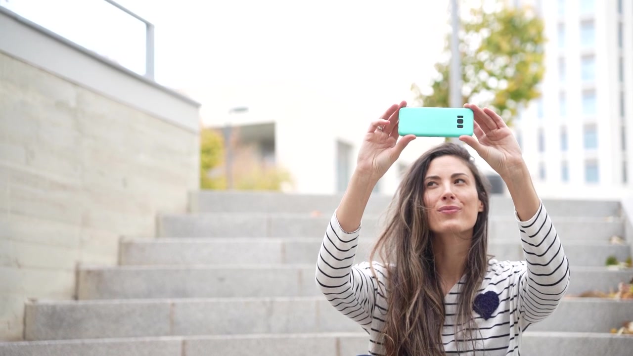 Uma jovem desfrutando alegremente um momento de selfie enquanto sentada em degraus externos.