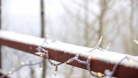 close up of white christmas lights on a snowy deck with aspen trees in the background and snow falling