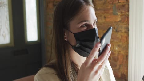 caucasian female customer wearing face mask, sitting at table, using smartphone