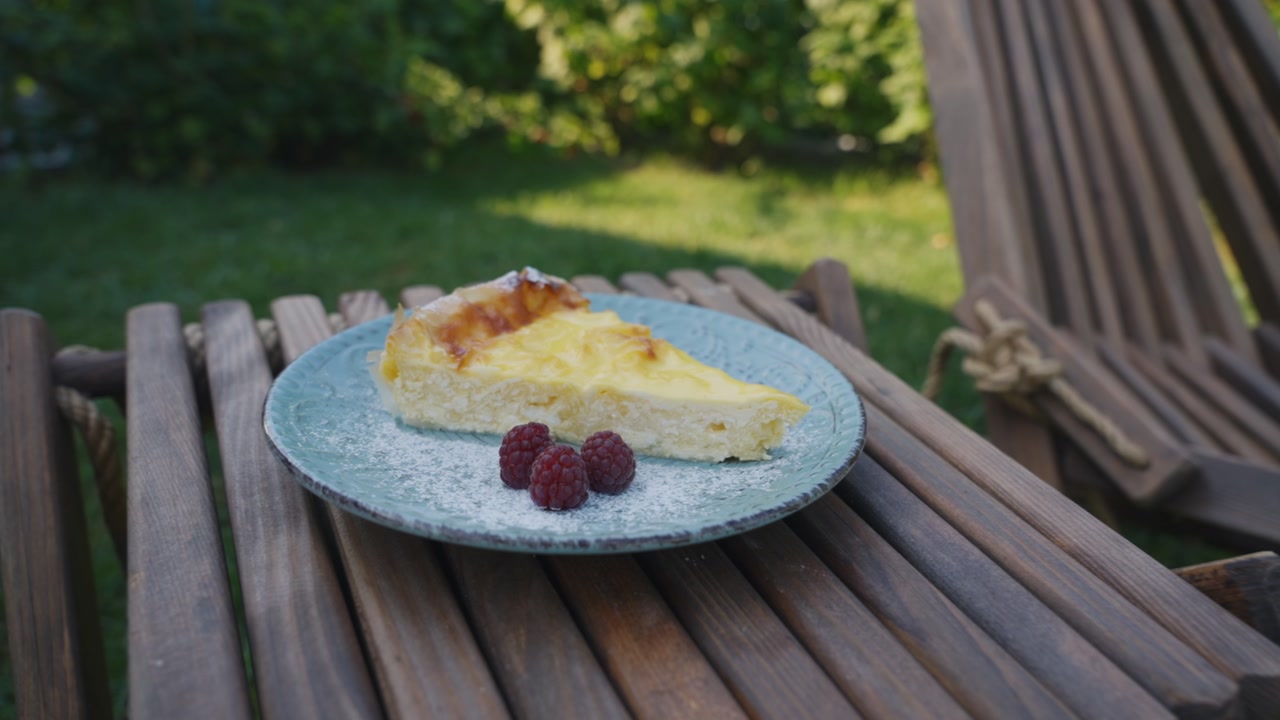 Slice of cake served with raspberries on plate in outdoor garden setting