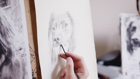 close up of artist sitting at easel drawing picture of dog in charcoal