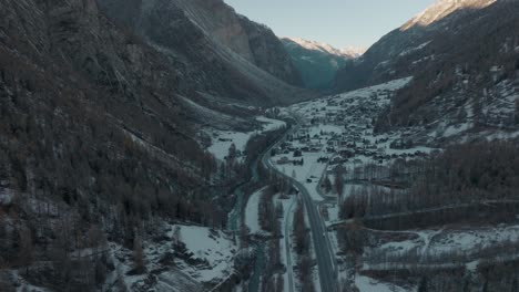 forward aerial in snowy river valley in epic swiss alps with stunning alpine mountain panorama and lush pine forests on hillsides