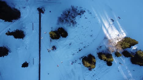 top down static shot of a busy mountain resort with skiers and snowboarders on a ski slope and children lining up to take a magic carpet lift and a chairlift running overhead near sofia, bulgaria