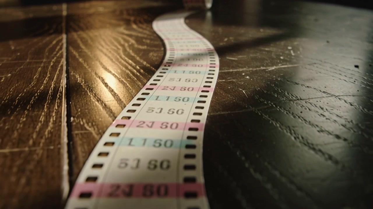 Camera tracking forward along perforated calibration strip on dark wood table, revealing metal roll