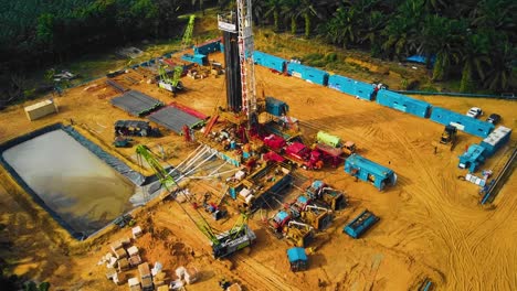 cinematic onshore drilling and workover rig structure and rig equipment for oil exploration and exploitation in the middle of jungle surrounded by palm oil trees during sunset time.