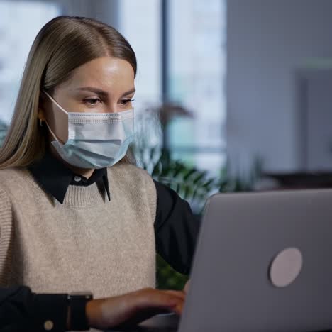 woman wearing surgical mask work at her laptop. beautiful lady in mask working in office. office work at quarantine period