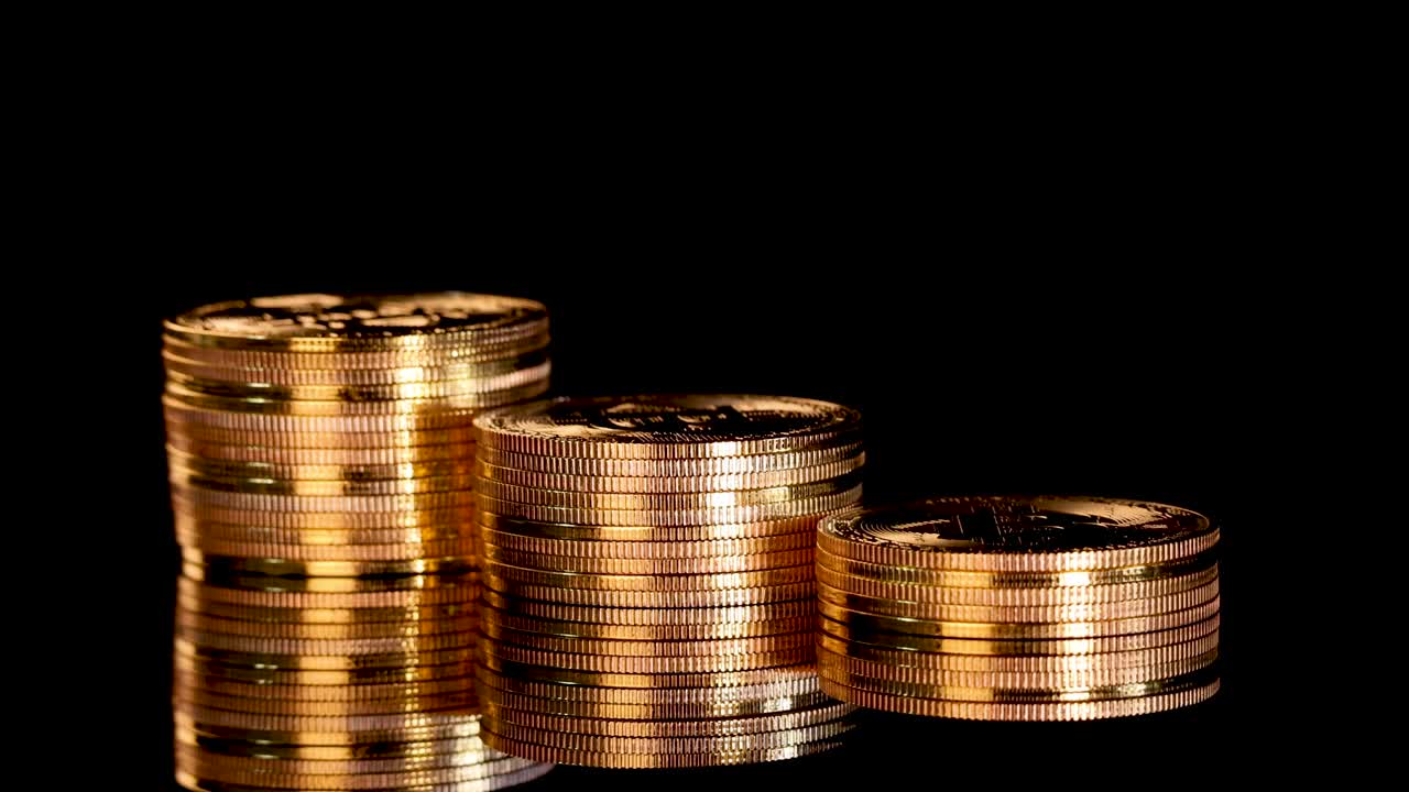 Stacks of shiny gold coins rotate smoothly, dramatically lit against a seamless black background