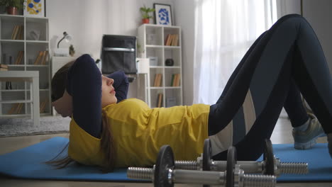 teen girl is training abdominal muscles lifting torso to knees lying on floor workout in living room of apartment sporty and healthy lifestyle fitness at home