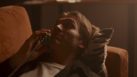 young man lying on sofa, having conversation on vintage phone