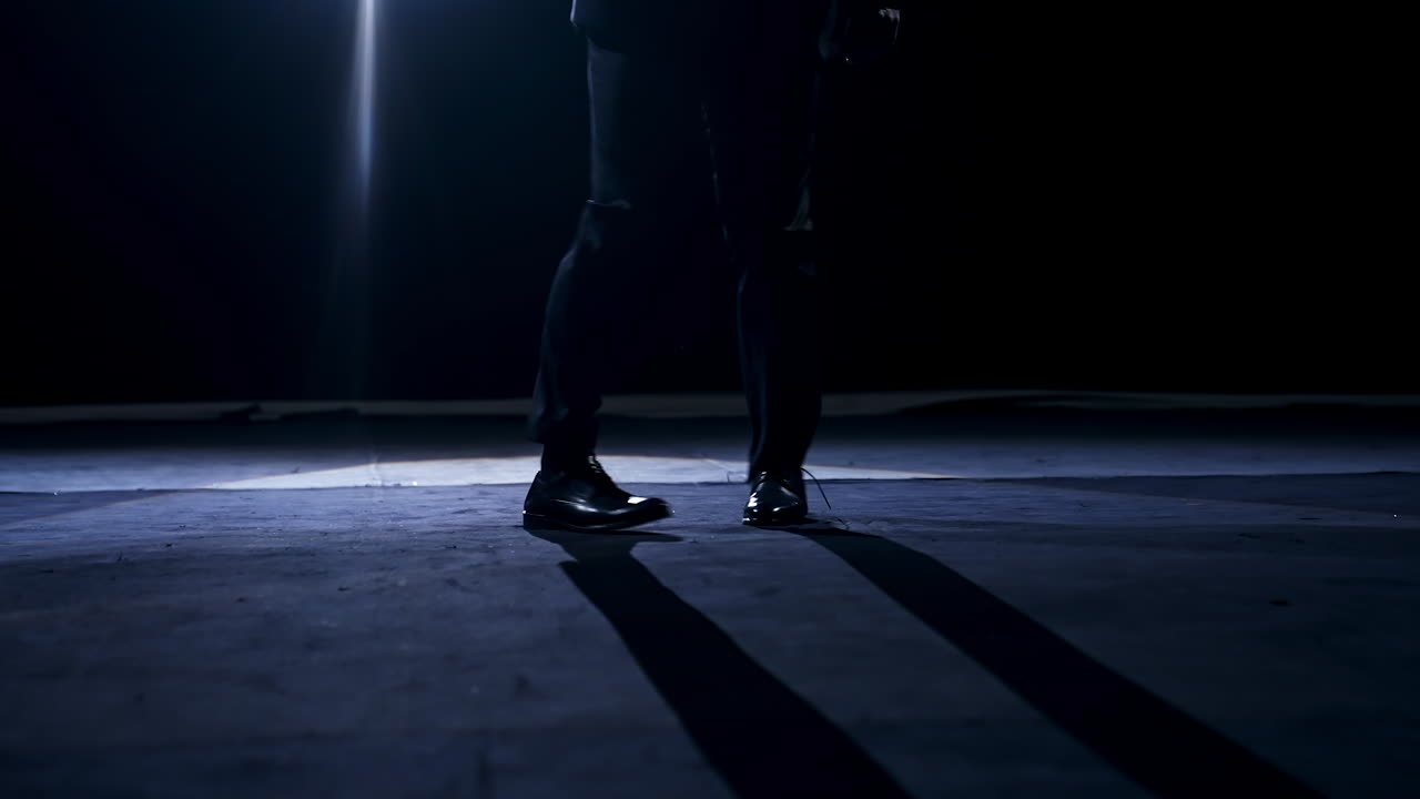 Legs of a dancer in move. Man in trousers and shoes dancing on the stage in dark scenic light.