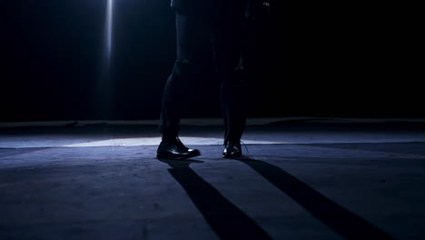 legs of a dancer in move. man in trousers and shoes dancing on the stage in dark scenic light.