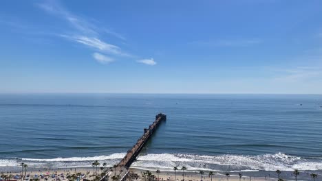 rising drone shot off the oceanside beach pier on a sunny day with blue sky and some white clouds