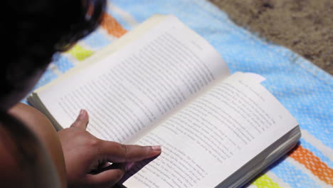 overhead view of a person engrossed in reading a book on a vibrant beach blanket