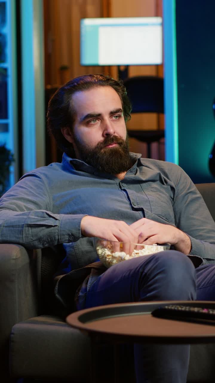 Vertical video Sad man on couch eating popcorn from stress while watching drama movie