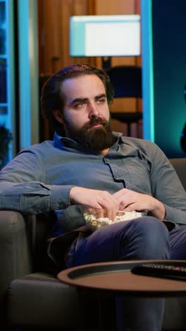 vertical video sad man on couch eating popcorn from stress while watching drama movie