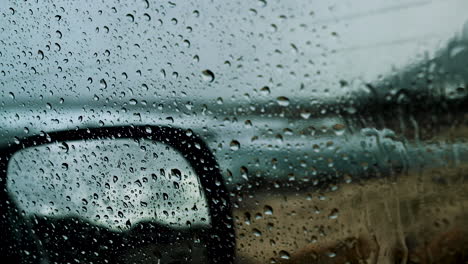 Fat-raindrops-on-car-window-on-rainy-day,-blurry-ocean-waves-in-background