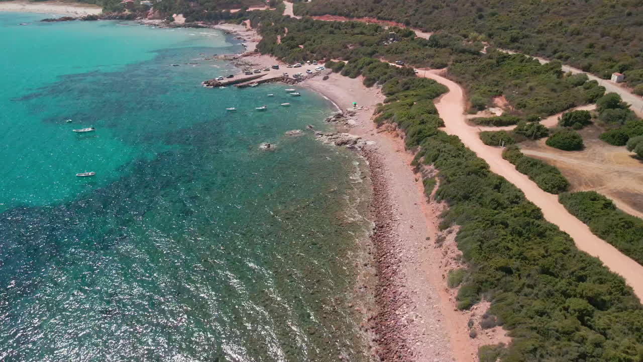 Mare tropicale blu con barche ormeggiate vicino a un paesaggio costiero sabbioso con vegetazione durante una giornata di sole in Sardegna, Italia