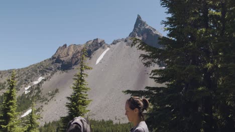 Girl-and-black-lab-taking-a-break-on-hike-with-pointed-mountain-in-the-background