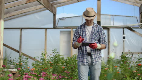 el joven empresario propietario de un invernadero está haciendo un inventario en el invernadero contando plantas y ingresando información en la tableta. el hombre atractivo está ocupado comprobando la vegetación.