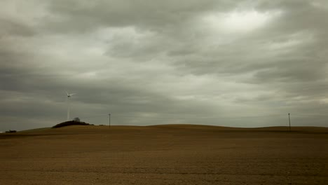 la turbina de viento blanca en la cima de una colina forma el telón de fondo de un paisaje de campo vasto desolado y desolado salpicado de postes telefónicos bajo un cielo nublado