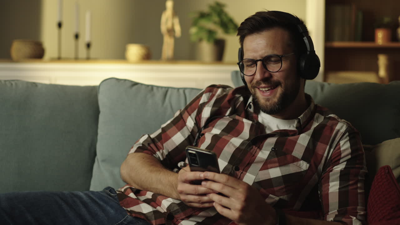 Man relaxing on couch with headphones and mobile phone