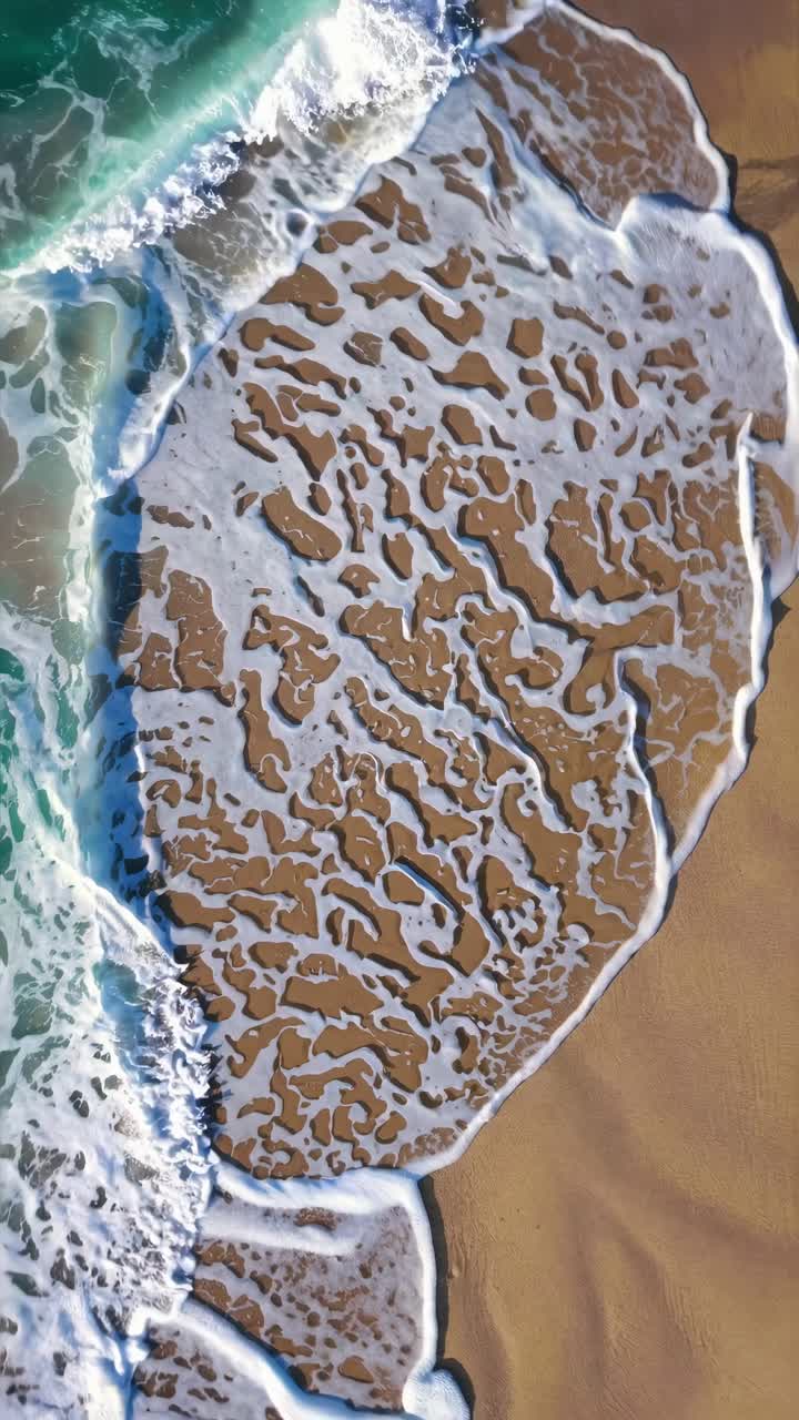 Aerial view of abstract sand patterns and ocean waves. The video captures a top-down angle