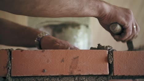 closeup view on a man fills in a space between bricks with a cement solution by naked hands. a repairman is building a wall with bricks