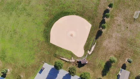 high aerial rotating shot of empty baseball field, no people, in rural countryside in summer, home of little league