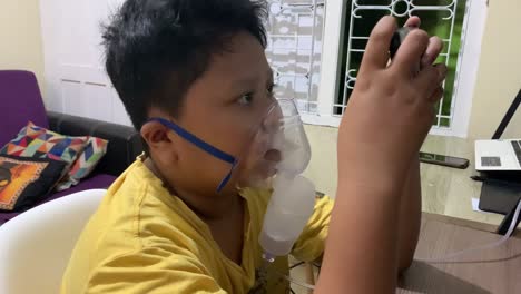 asian boy use inhaler nebulizer while playing game with his smartphone