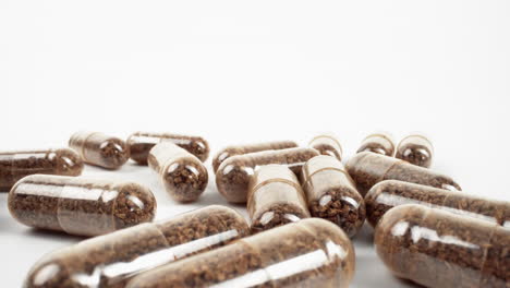 transparent capsules with brown herbal powder on a white backdrop