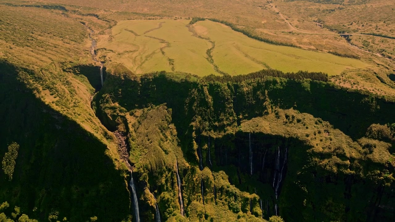 Vista aérea de múltiplas cachoeiras caindo por penhascos exuberantes em um vale verde em Flores