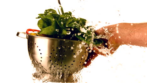 water pouring over salad in colander held by hand