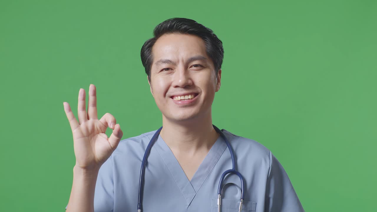 스테토스코프를 들고 있는 아시아 남성 의사의 근접 사진. 병원의 녹색 스크린 배경에서 은 몸짓과 웃음을 보여준다.