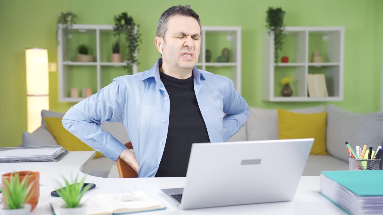 Home office worker man experiencing back pain due to sitting disorder.