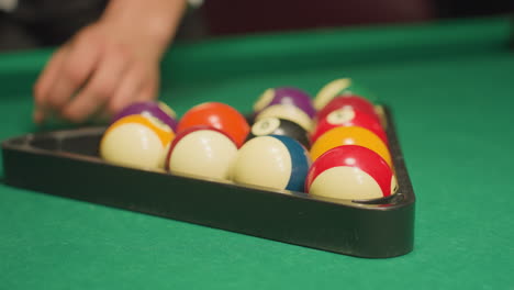 close-up shot of man's hand carefully placing billiard balls into triangle rack on green pool table, aligning them for perfect setup before break shot. focus on precision, strategy